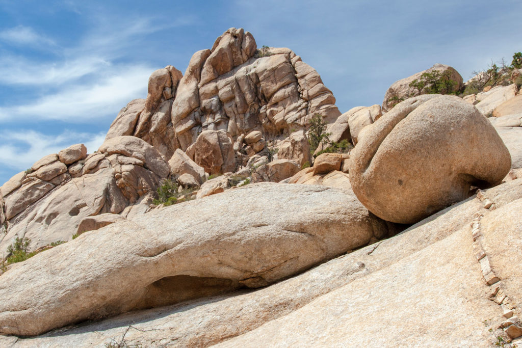 creased boulder resting on a slab before a crest of rocks beneath a blue sky